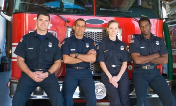 Four firefighters standing confidently in front of a fire truck.